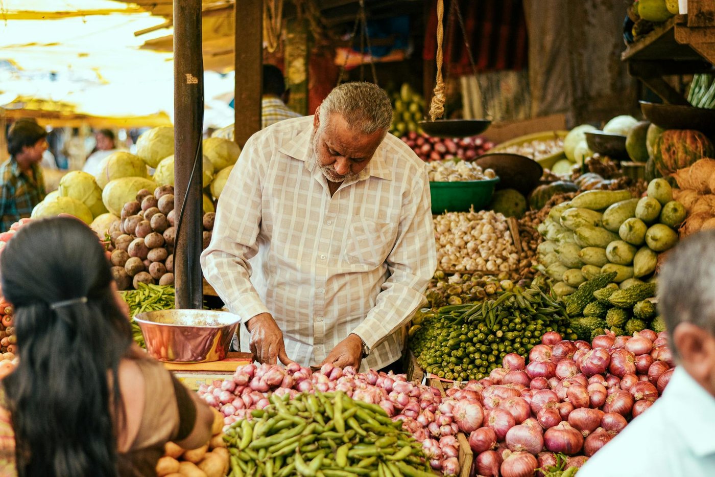 Old ethnic salesman selling onion green beans cabb