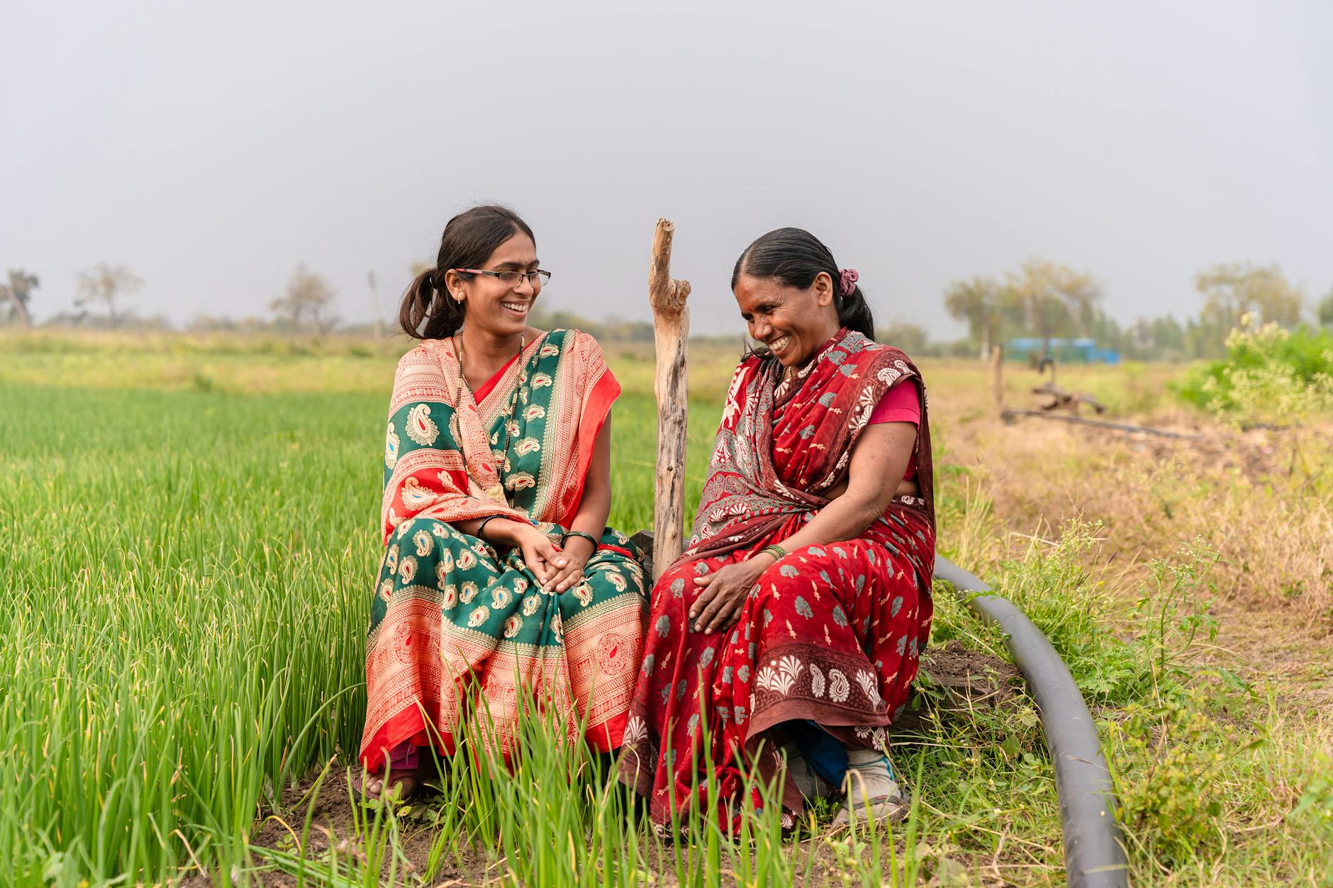 Two smiling Indian women in colorful sarees in a field